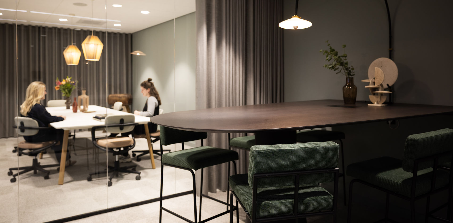 Lichte moderne kantoorruimte met houten stoelen, grote kamerplanten en een vrouw aan de telefoon